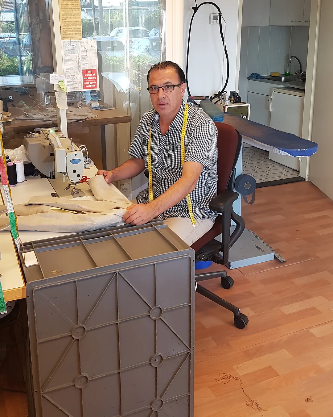 Rafo aan de naaimachine in zijn werkplaats, met een meetlint om zijn nek
