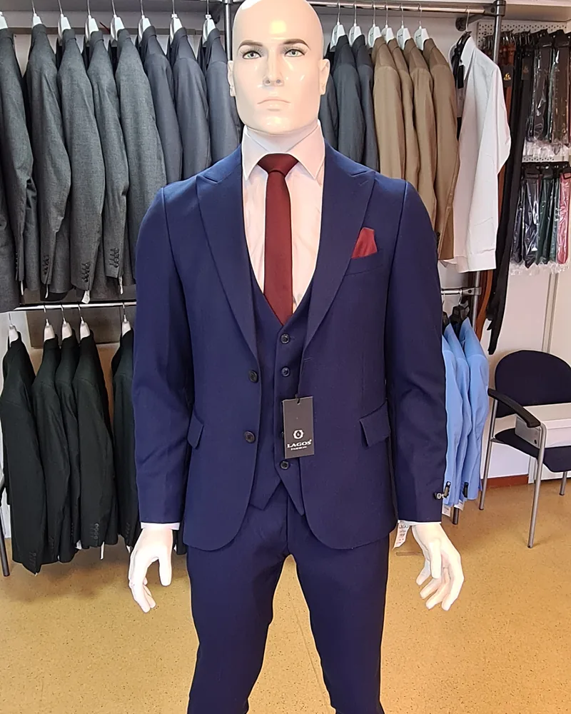 Een donkerblauw driedelig kostuum met bordeauxrode stropdas op een paspop
